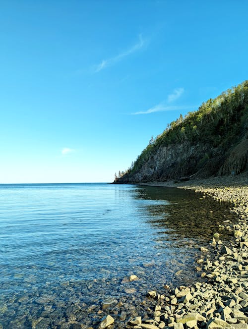 View of Rocks on a Beach, Hill and Body of Water under Blue Sky