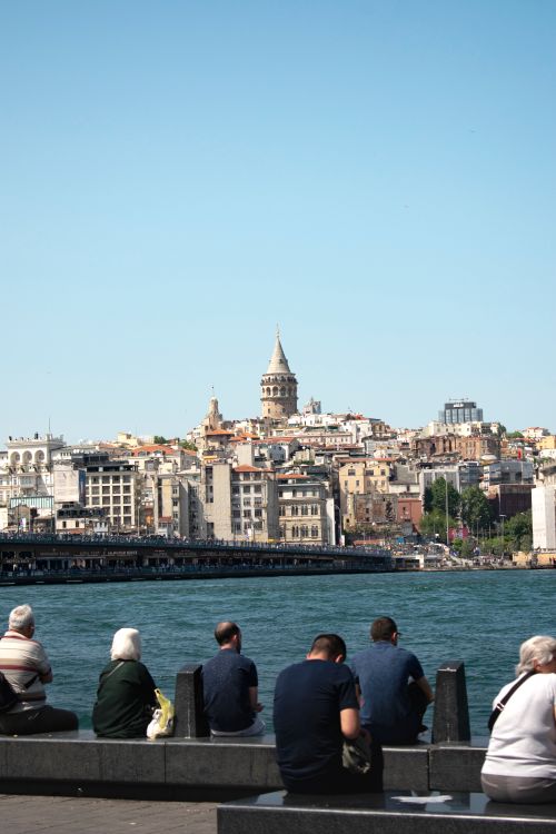 Free People sitting by the sea with Galata Tower and Istanbul cityscape in the background. Stock Photo