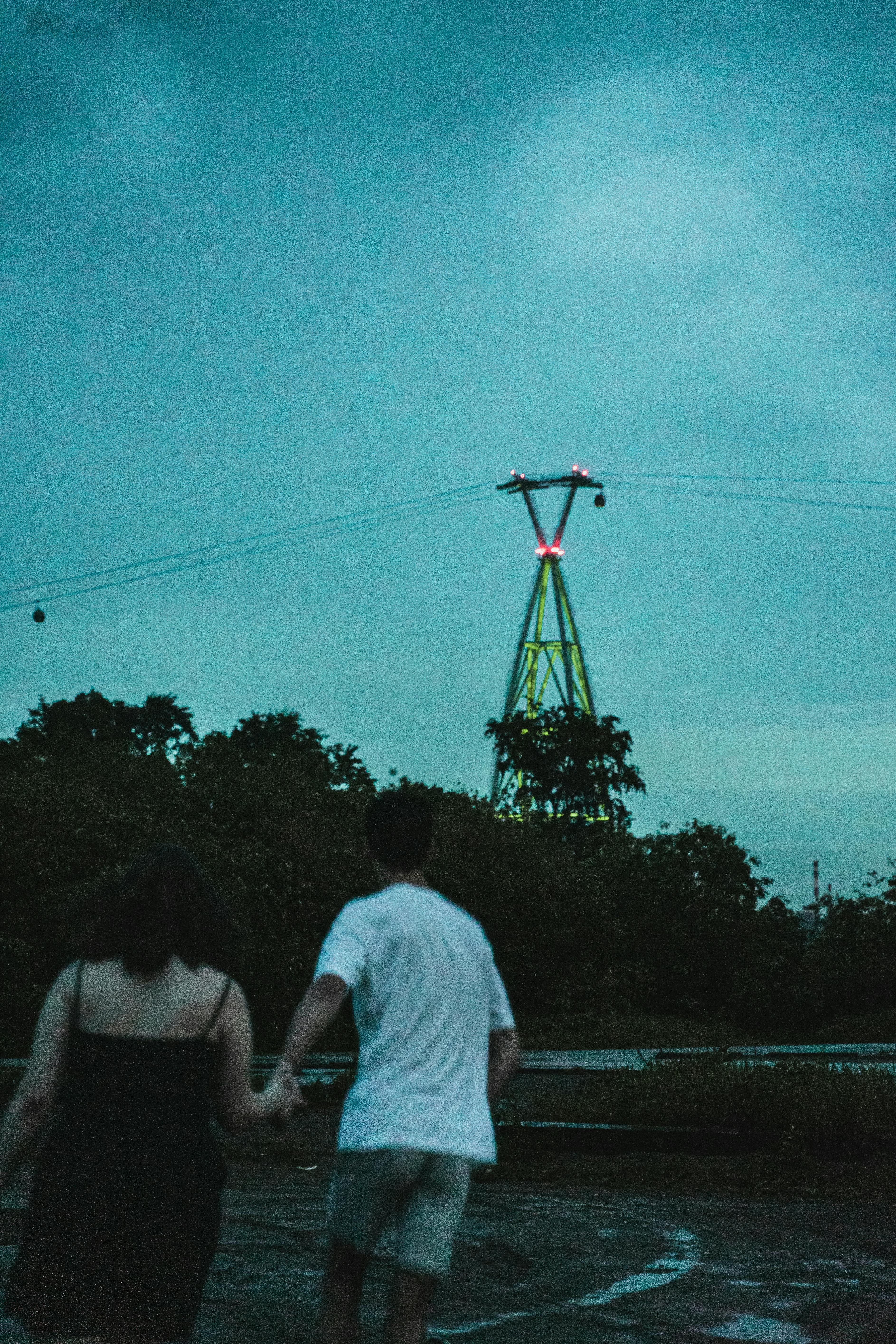 Silhouettes of a couple walking beneath a cloudy night sky near power lines with trees in the background.