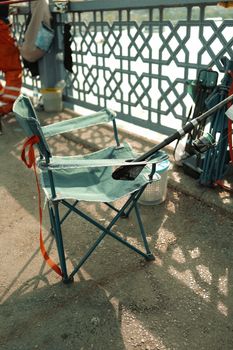 A folding fishing chair with a rod and gear on a bridge, perfect for relaxation by the water.