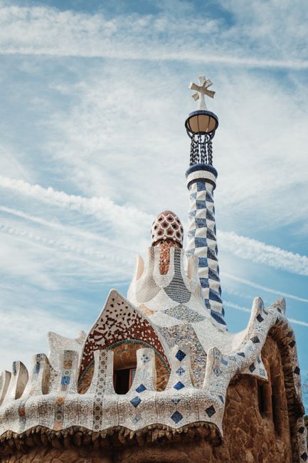 Explore the vibrant mosaic tower of Park Güell against a blue sky in this iconic Barcelona scene.