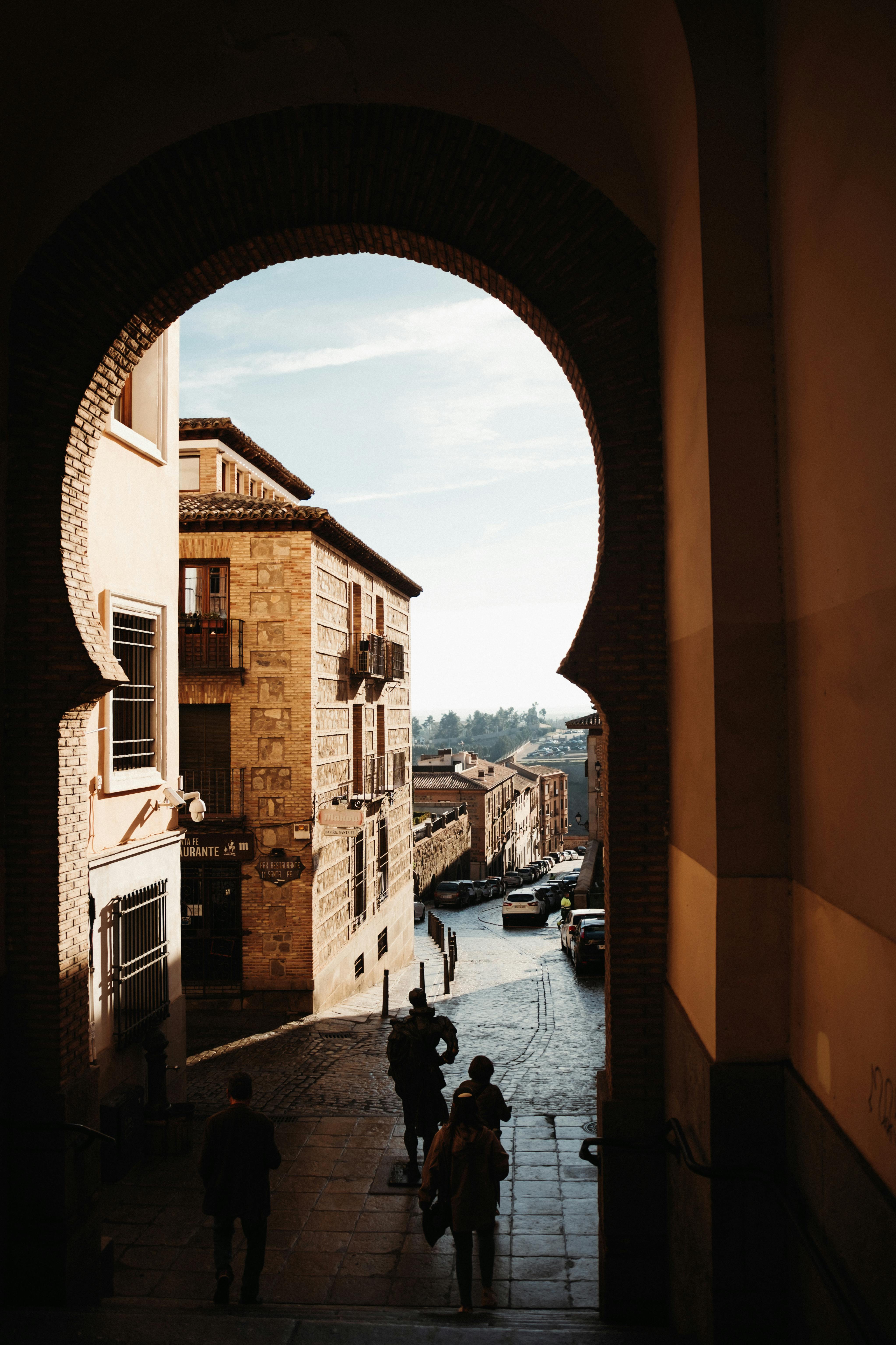 View through an ancient arch in Toledo, Spain, showcasing historic architecture and a narrow cobblestone street.