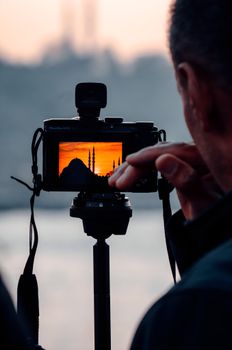 A photographer captures a vibrant sunset view of an iconic mosque in İstanbul, Türkiye, through a camera screen.