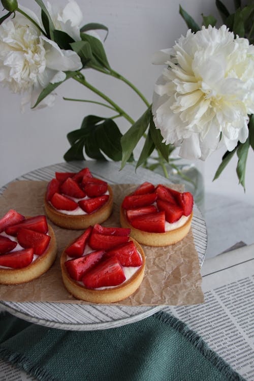 Single Serve Tarts with Strawberries Served on Wooden Plate next to White Flowers in Vase