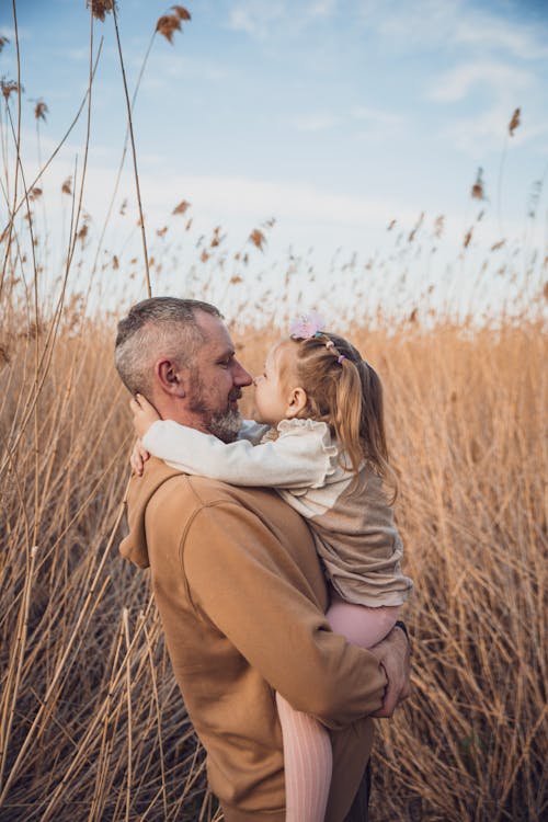 Free A Man Holding his Little Daughter while Standing in a Field Stock Photo