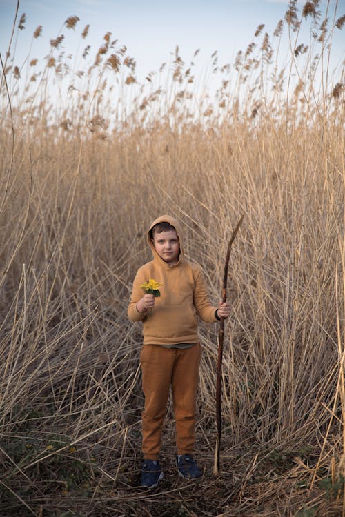 Boy in Hoodie with Wooden Stick Standing by Field