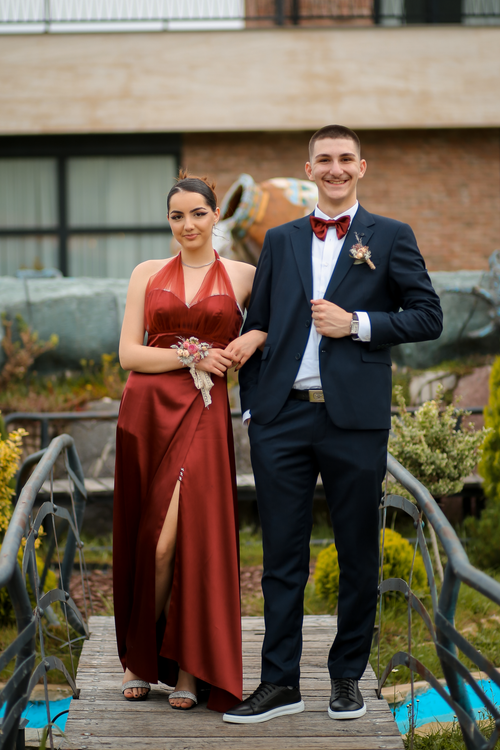 Free A well-dressed couple stands confidently on a footbridge, showcasing formalwear in an outdoor setting. Stock Photo