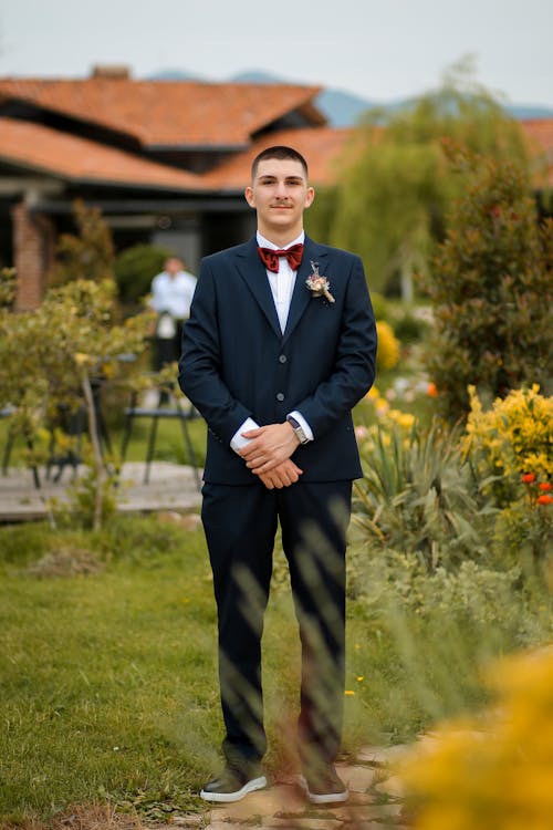Elegant Young Man in a Suit with a Bow Tie Standing in the Garden 