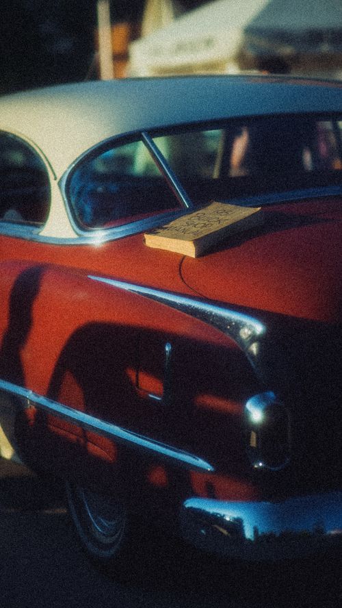 Free A vintage red Oldsmobile with a book on the trunk, captured in warm sunlight. Stock Photo