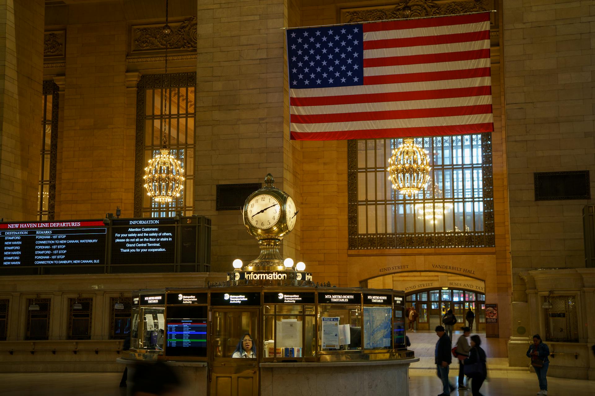 Interior view of Grand Central Terminal featuring the American flag and iconic clock under elegant chandeliers.