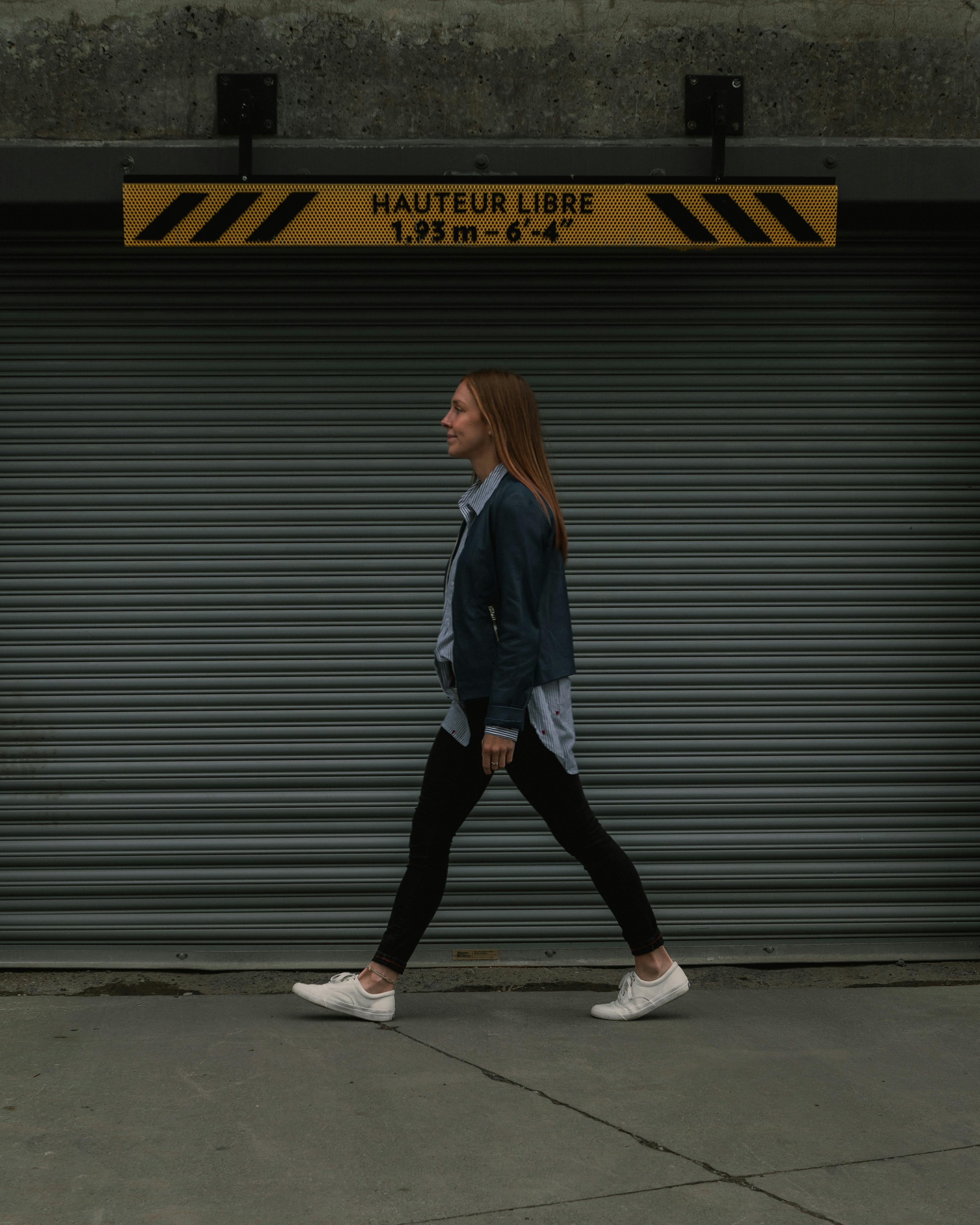 woman in jacket and shirt walking by garage doors in city