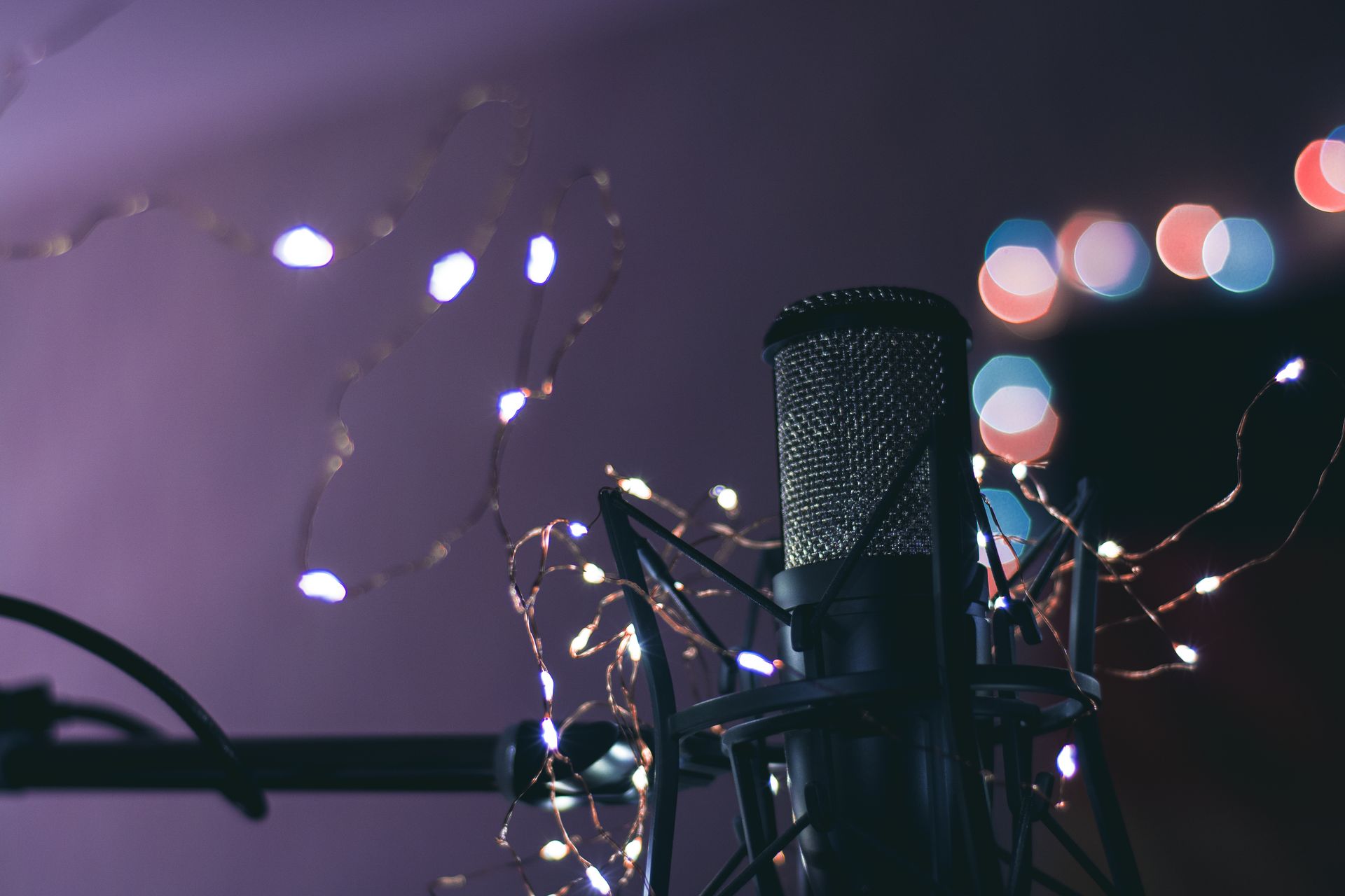 Condenser microphone surrounded by string lights creating a bokeh effect, ideal for studio and music themes.