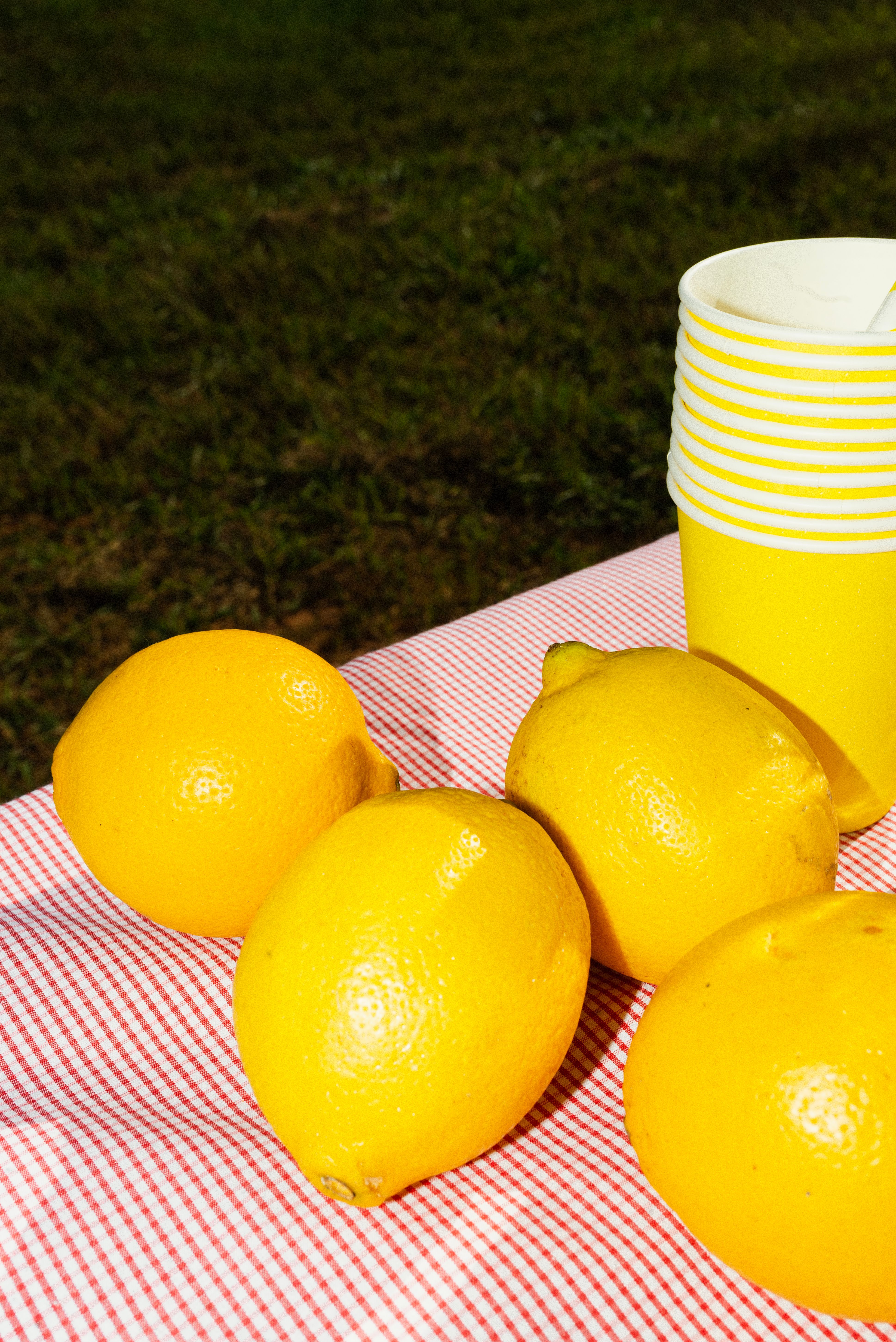 Close-up of fresh lemons on a picnic table with yellow cups, creating a vibrant outdoor scene.