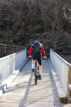 Cyclist with a backpack crossing a wooden footbridge outdoors, enjoying a sunny ride.