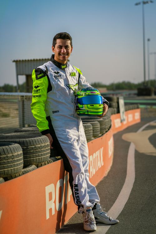 Free Race car driver in white and neon suit poses with helmet on racing track. Stock Photo