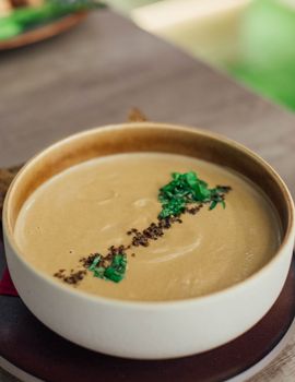 陶瓷碗里盛着美味的奶油汤，上面点缀着香草，放在木桌上