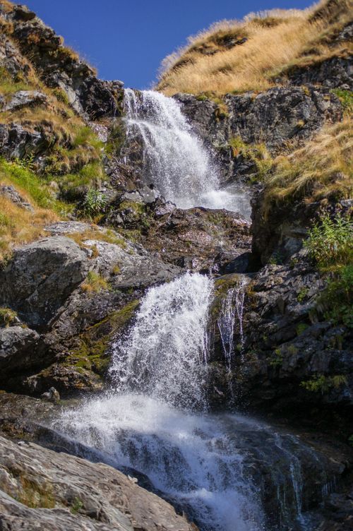 Free A serene waterfall flows over rocks with lush grass in a picturesque outdoor setting. Stock Photo
