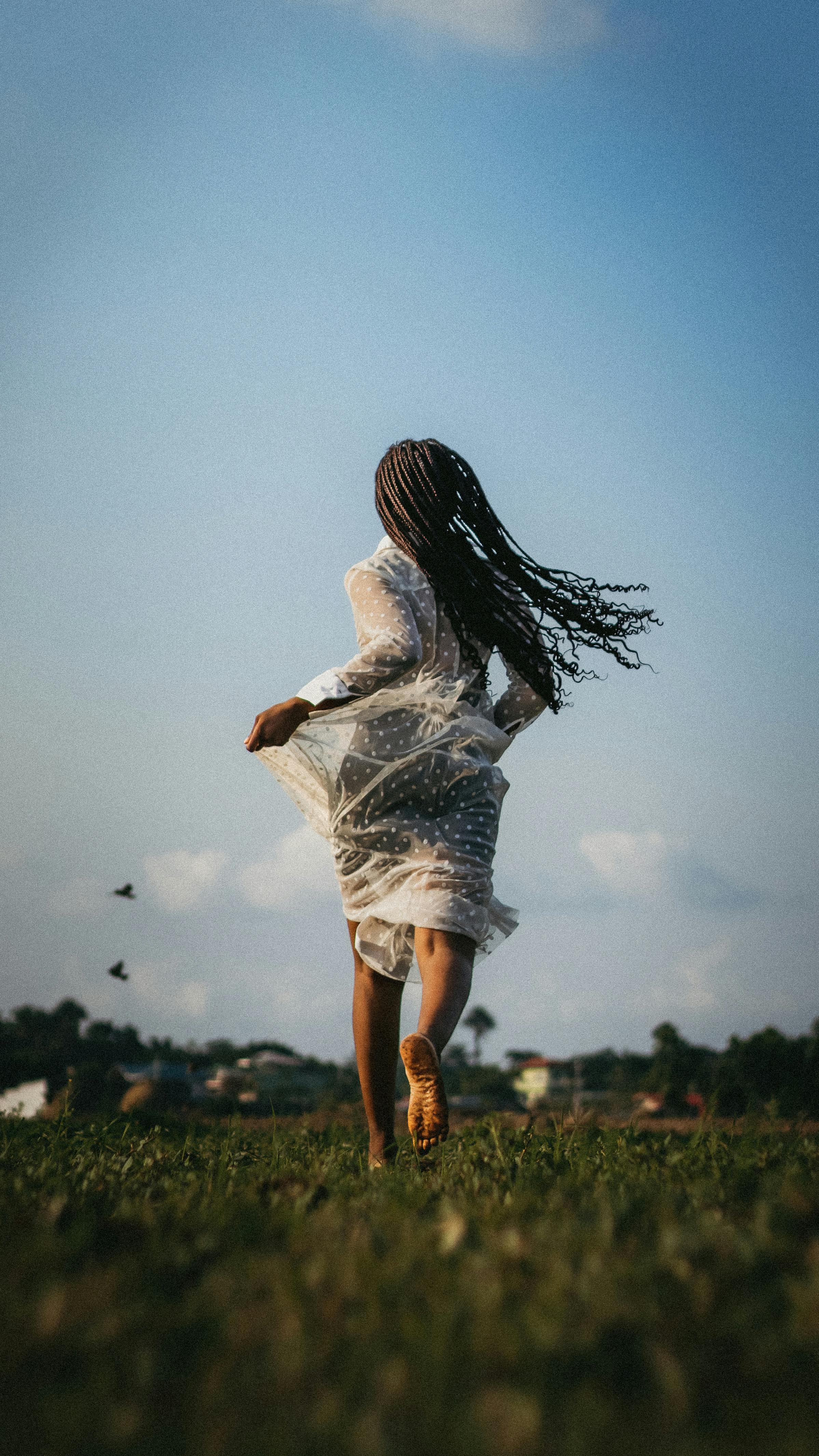 A woman in a dress runs barefoot through a grassy field on a sunny summer day.