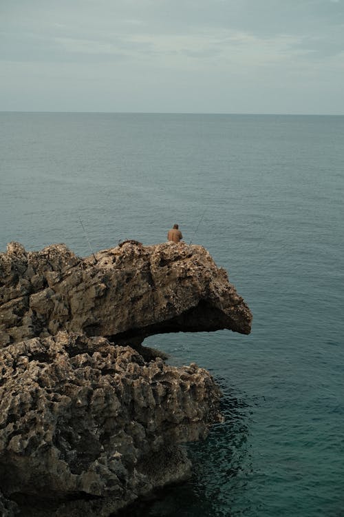 Angler Fishing on Rock Formation by Sea