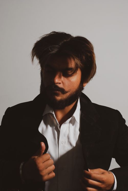 Free Portrait of a bearded man in a suit adjusting his collar, exuding confidence and style. Stock Photo
