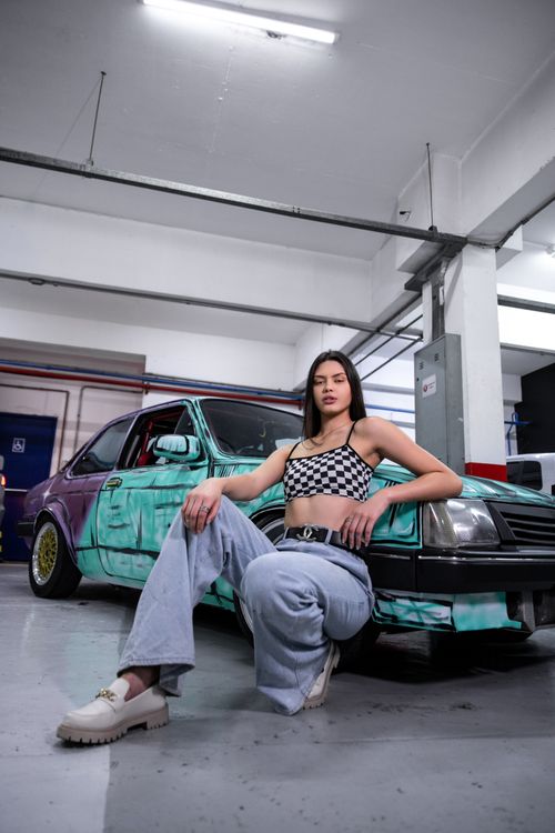 Free Trendy woman posing stylishly by a graffiti-covered car in a São Paulo garage. Stock Photo
