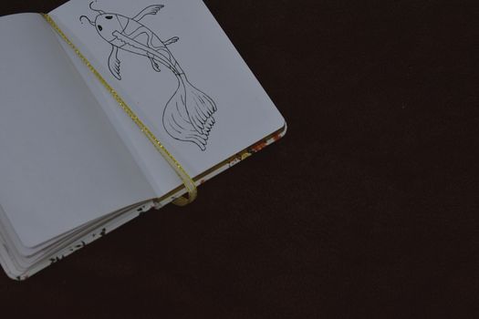 An open notebook showing a detailed fish sketch against a dark background.
