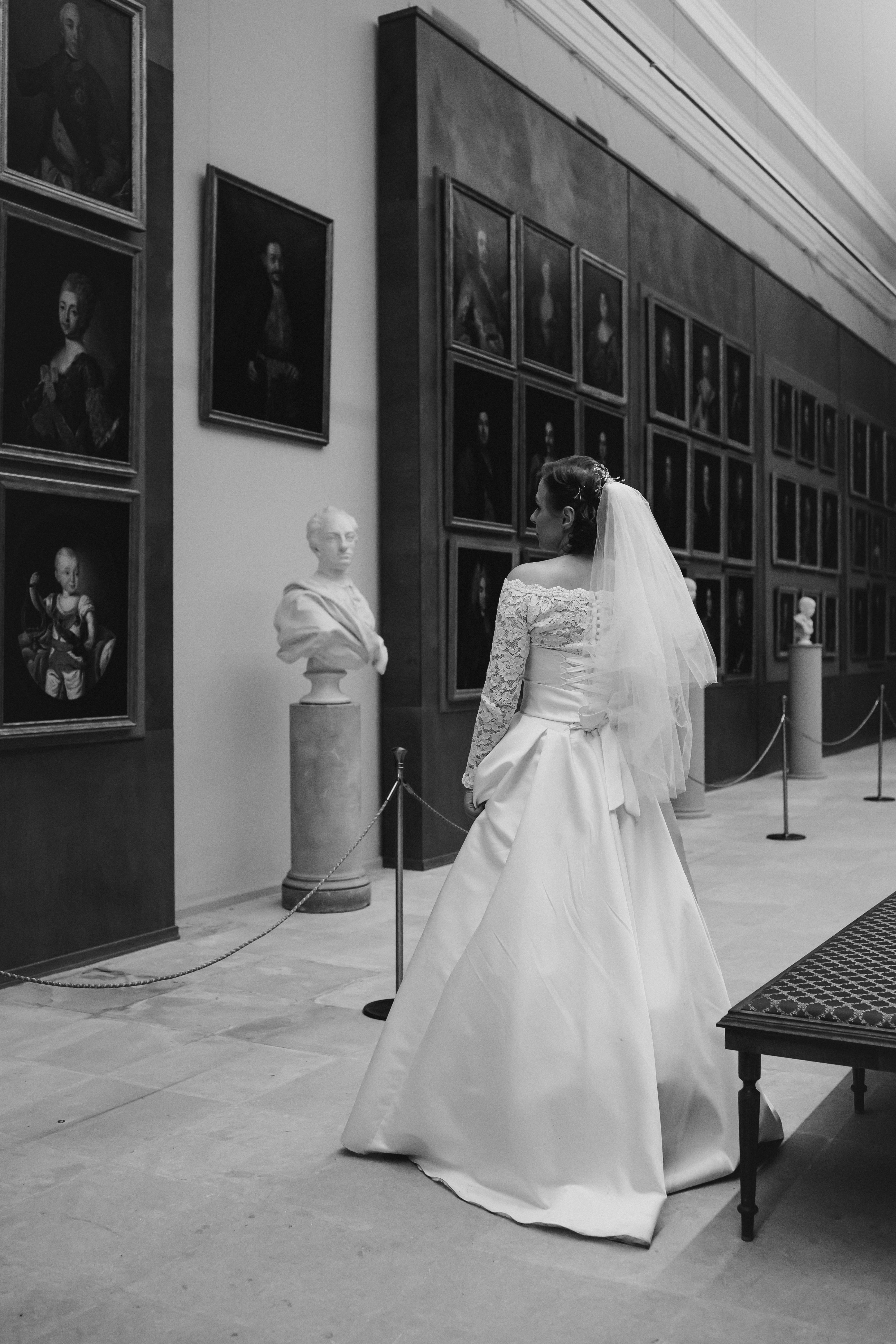 A bride in a wedding dress exploring an art gallery filled with classic portraits.