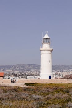 A scenic view of a white lighthouse standing tall against a coastal city backdrop.