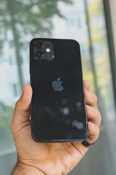 Close-up of a person holding a black smartphone outdoors with a blurred background.