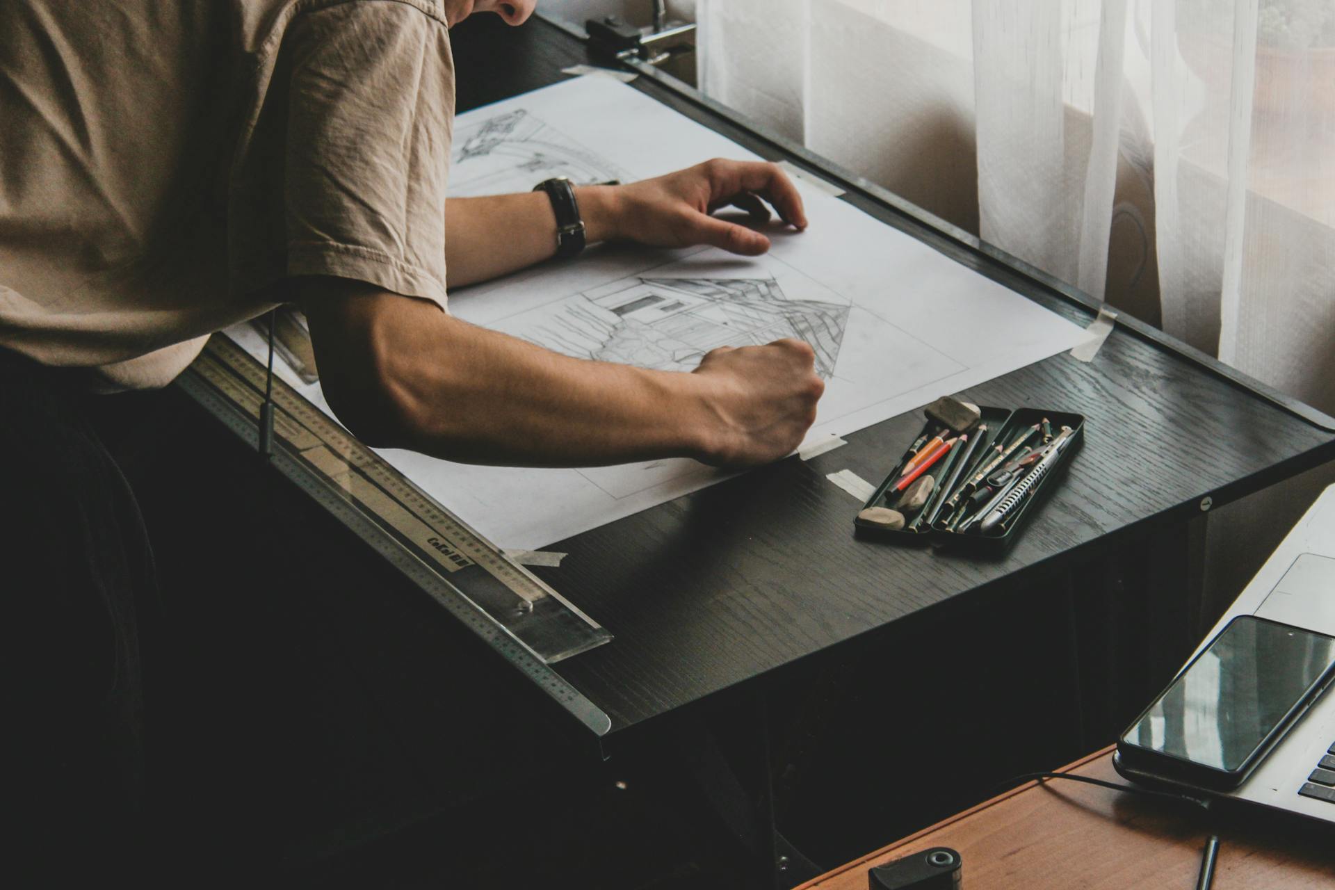 Close-up of an architect drafting designs on a desk with drawing tools.