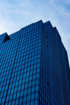 A modern skyscraper with reflective glass facade against a blue sky, showcasing urban architecture.