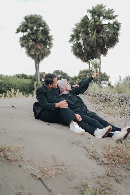 Free A couple in casual attire embracing on a beach with palm trees in the background. Stock Photo