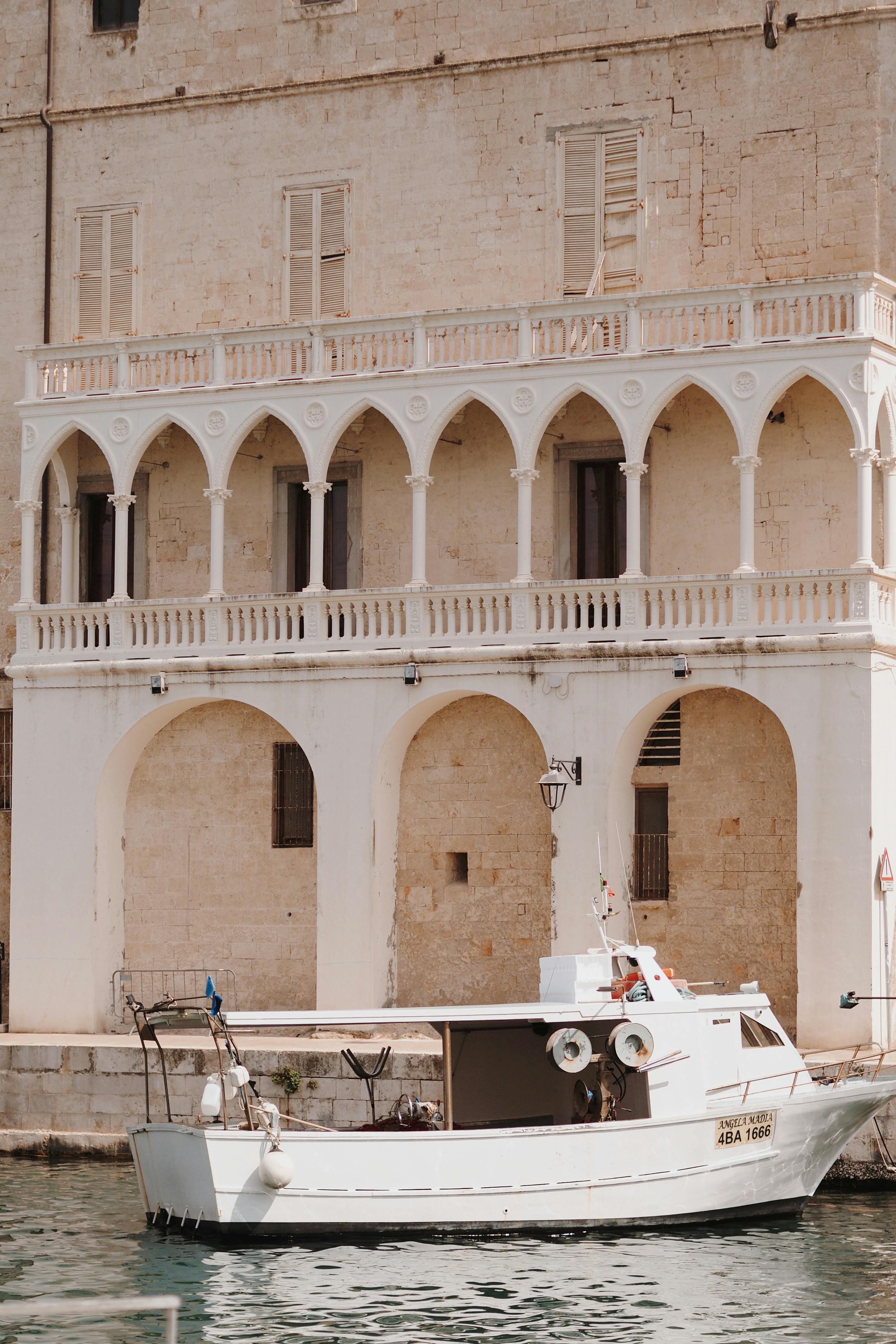 A picturesque stone building with arches stands by the water, with a boat moored in front.