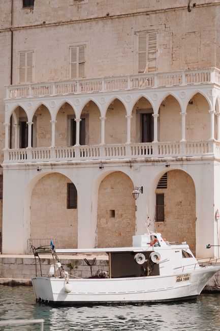 A picturesque stone building with arches stands by the water, with a boat moored in front.