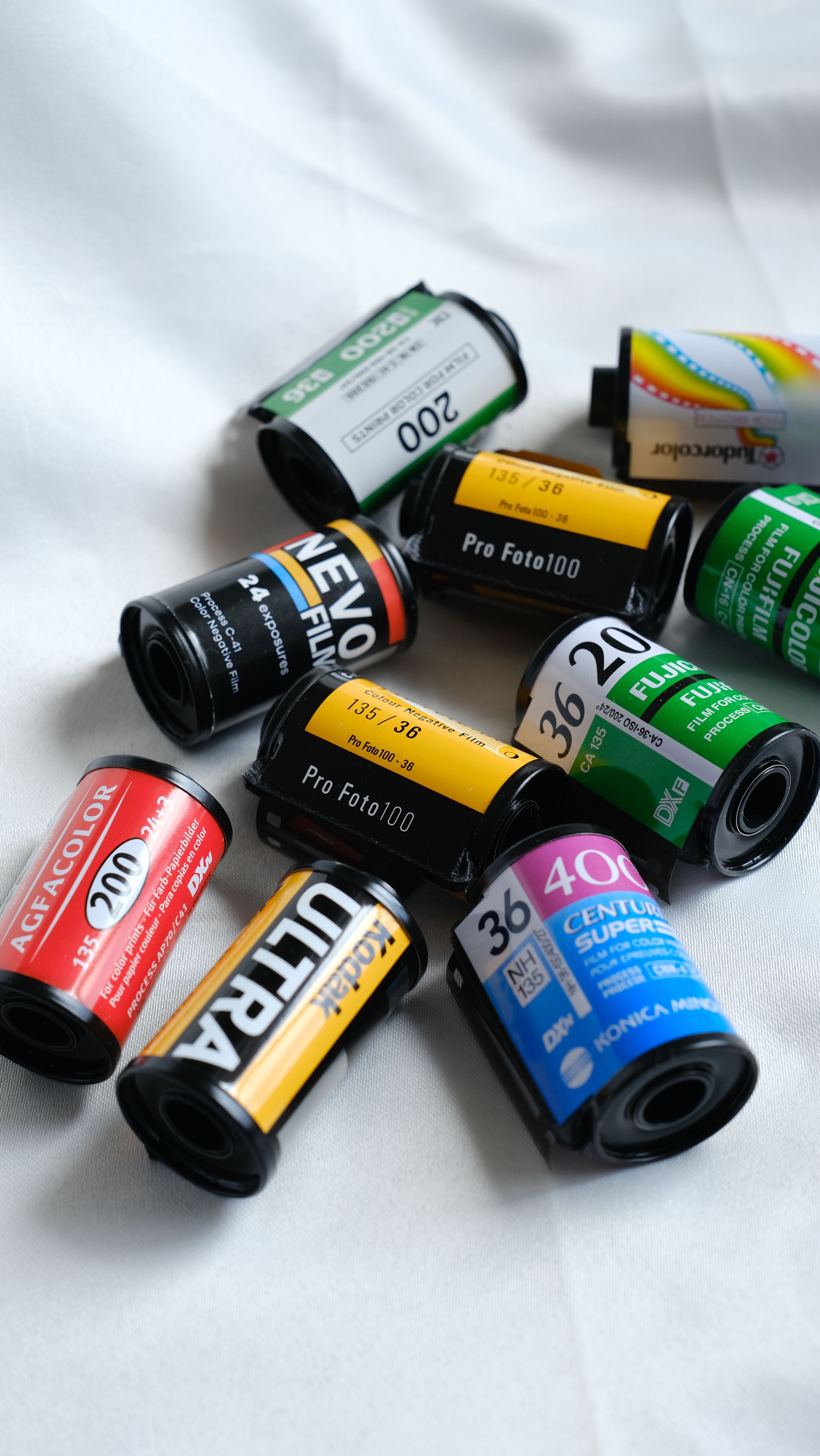 Collection of multi-colored vintage camera film rolls on a white cloth surface.