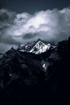 Moody mountain landscape with snow-capped peaks and dramatic cloud cover.