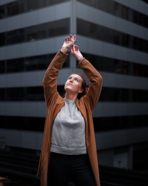 A fashionable woman poses confidently outdoors against a backdrop of modern architecture.