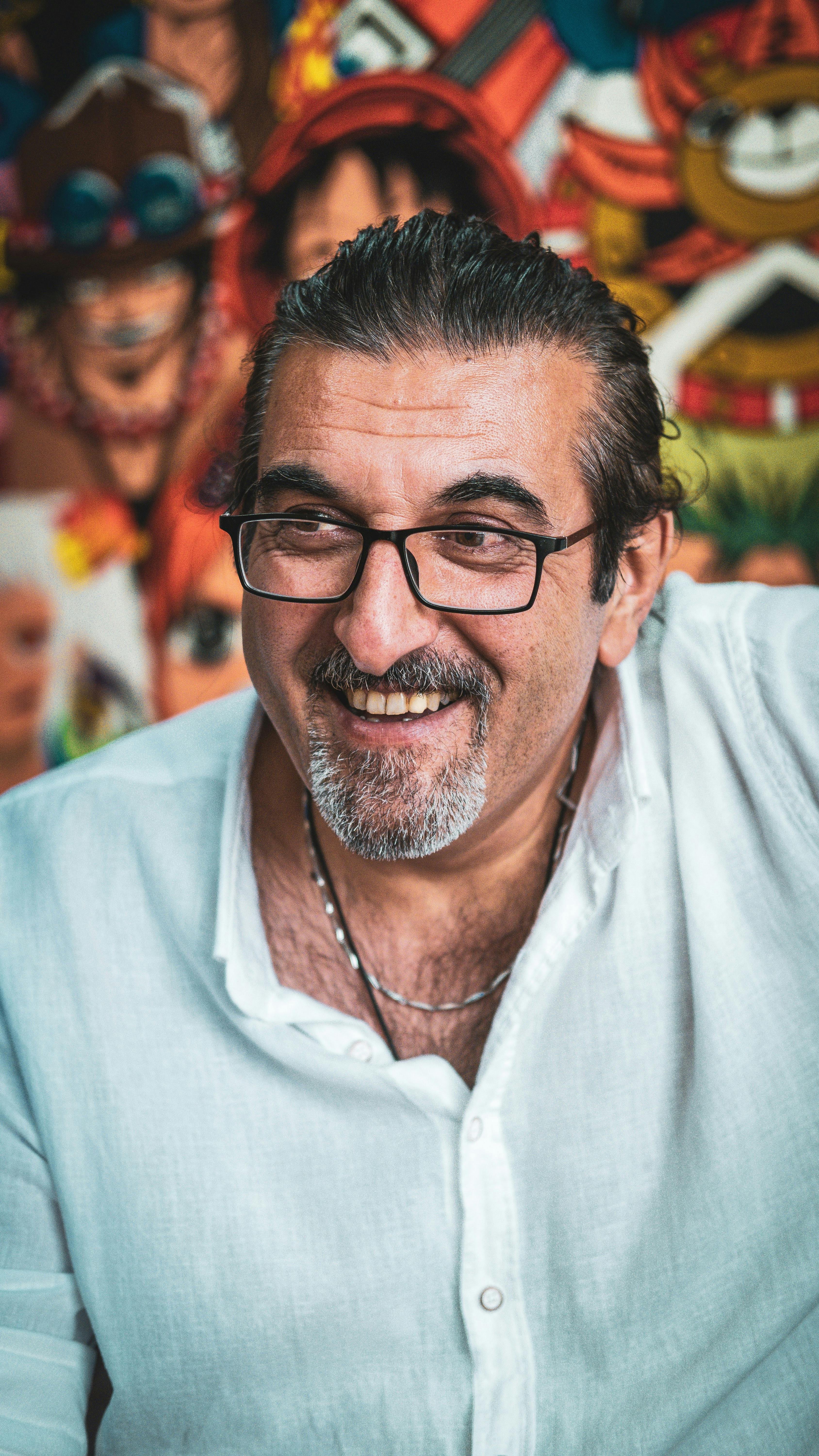 Middle-aged man in glasses smiling against a vibrant artistic background in Ankara.