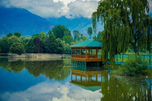Beautiful gazebo by a serene pond surrounded by lush trees, reflecting natural tranquility.