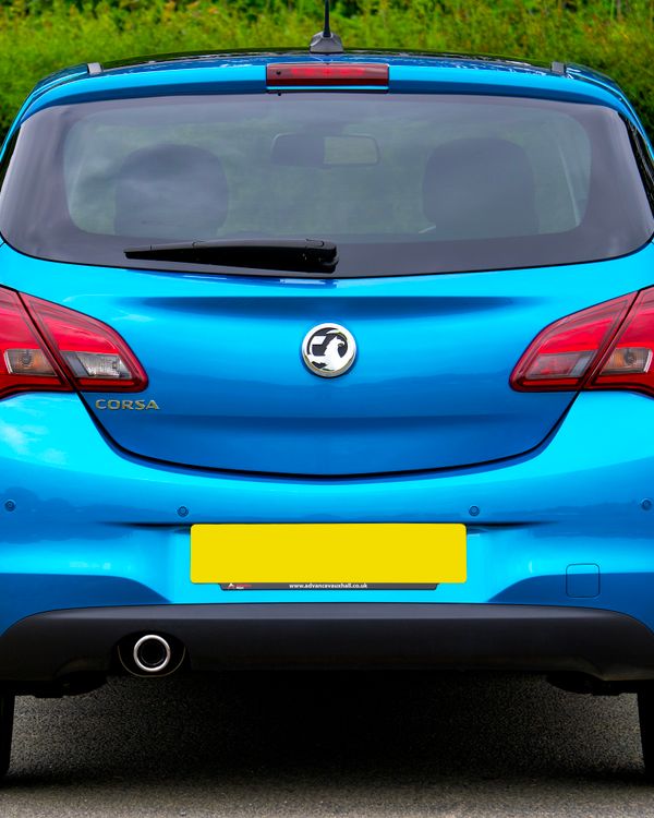 A blue hatchback car parked outdoors against a green background, showcasing its rear design.
