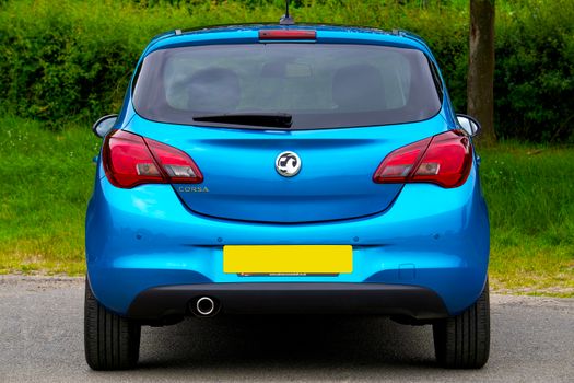 A blue hatchback car parked outdoors against a green background, showcasing its rear design.