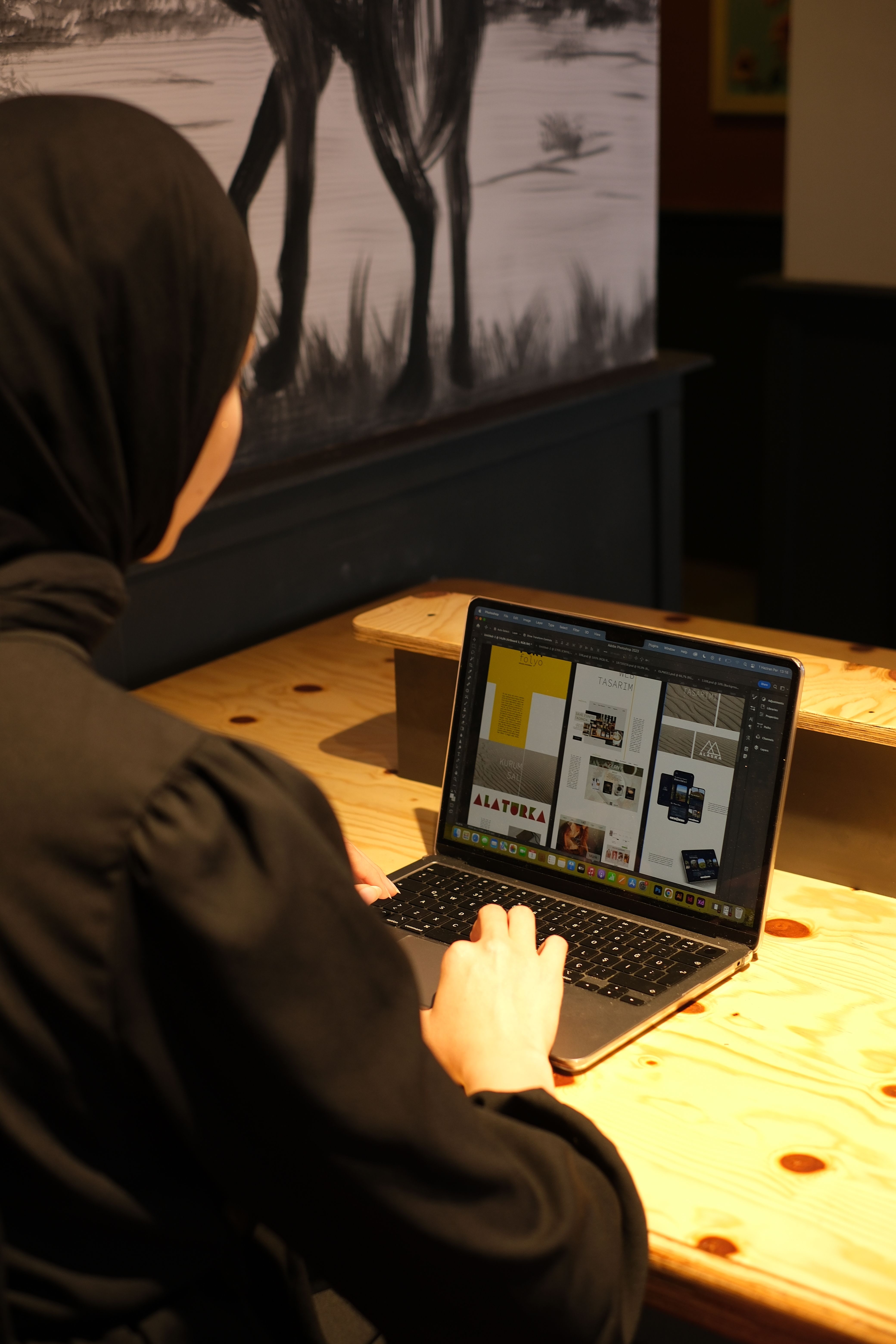 A woman wearing a hijab is working on a laptop in a cozy cafe setting, focused and productive.