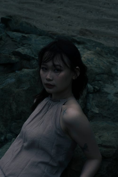 Young Brunette Woman in Gray Dress Lying on Rocks 