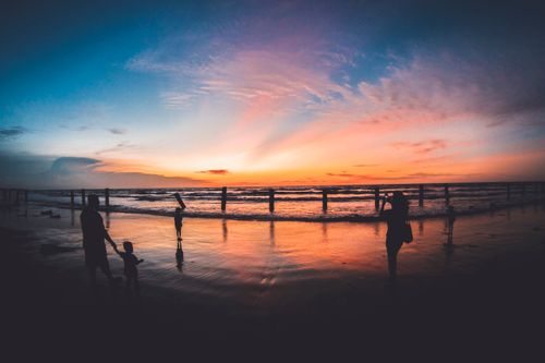 Free Silhouettes of people enjoying a serene sunset on the beach with vibrant sky reflection. Stock Photo