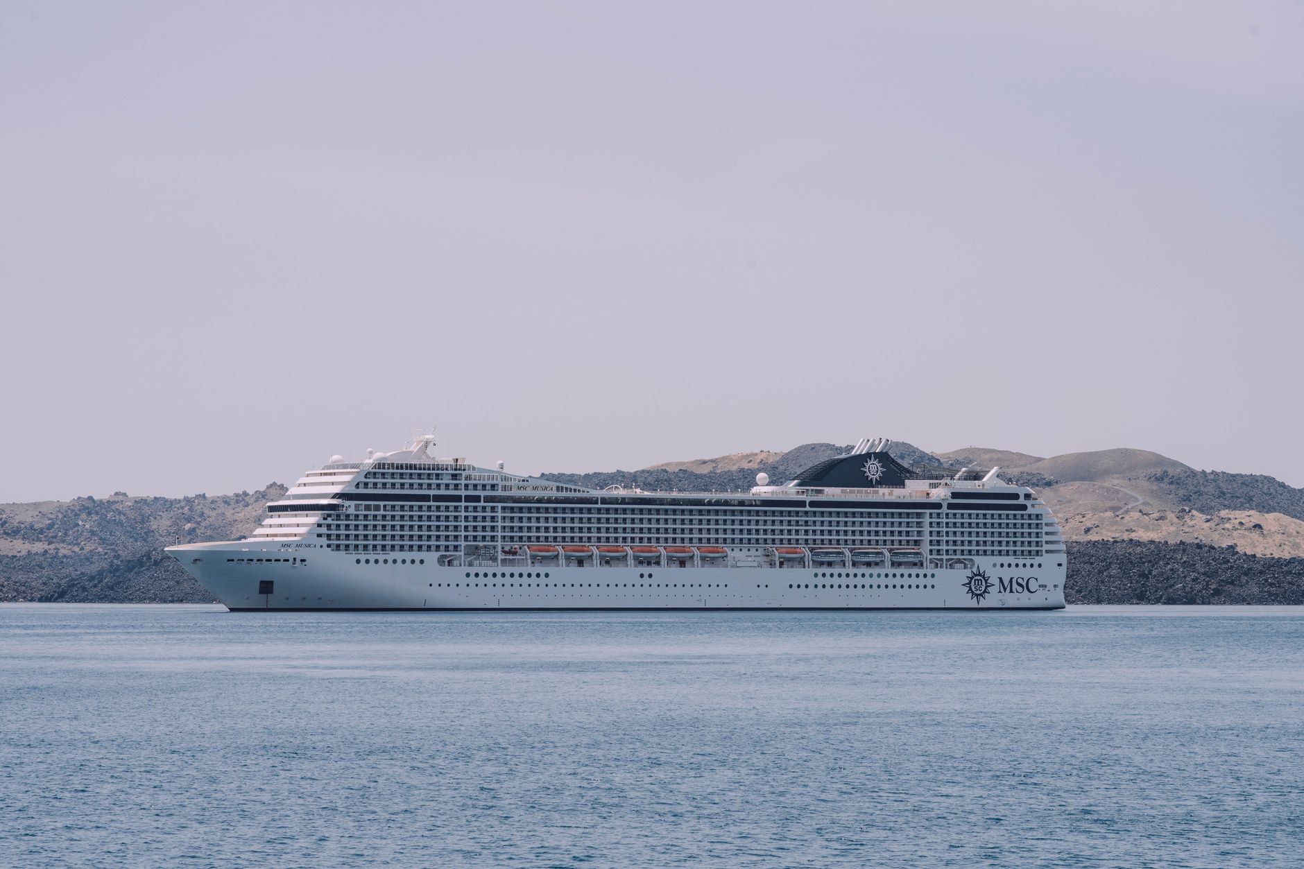 Weißes MSC-Kreuzfahrtschiff, das friedlich auf dem Meer fährt, mit einer malerischen Küstenlandschaft im Hintergrund.