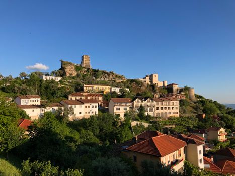 Picturesque view of Kruje Castle with hillside houses and lush greenery under a clear blue sky.