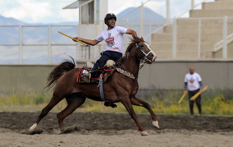 Man In Protective Helmet Riding A Horse And Launching A Wooden Stick While At A Jereed Competition