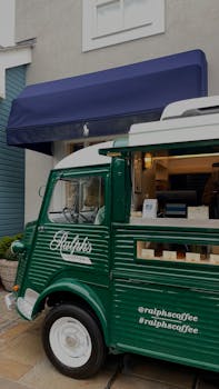 Green vintage coffee truck parked near a café on city streets, offering coffee on the go.