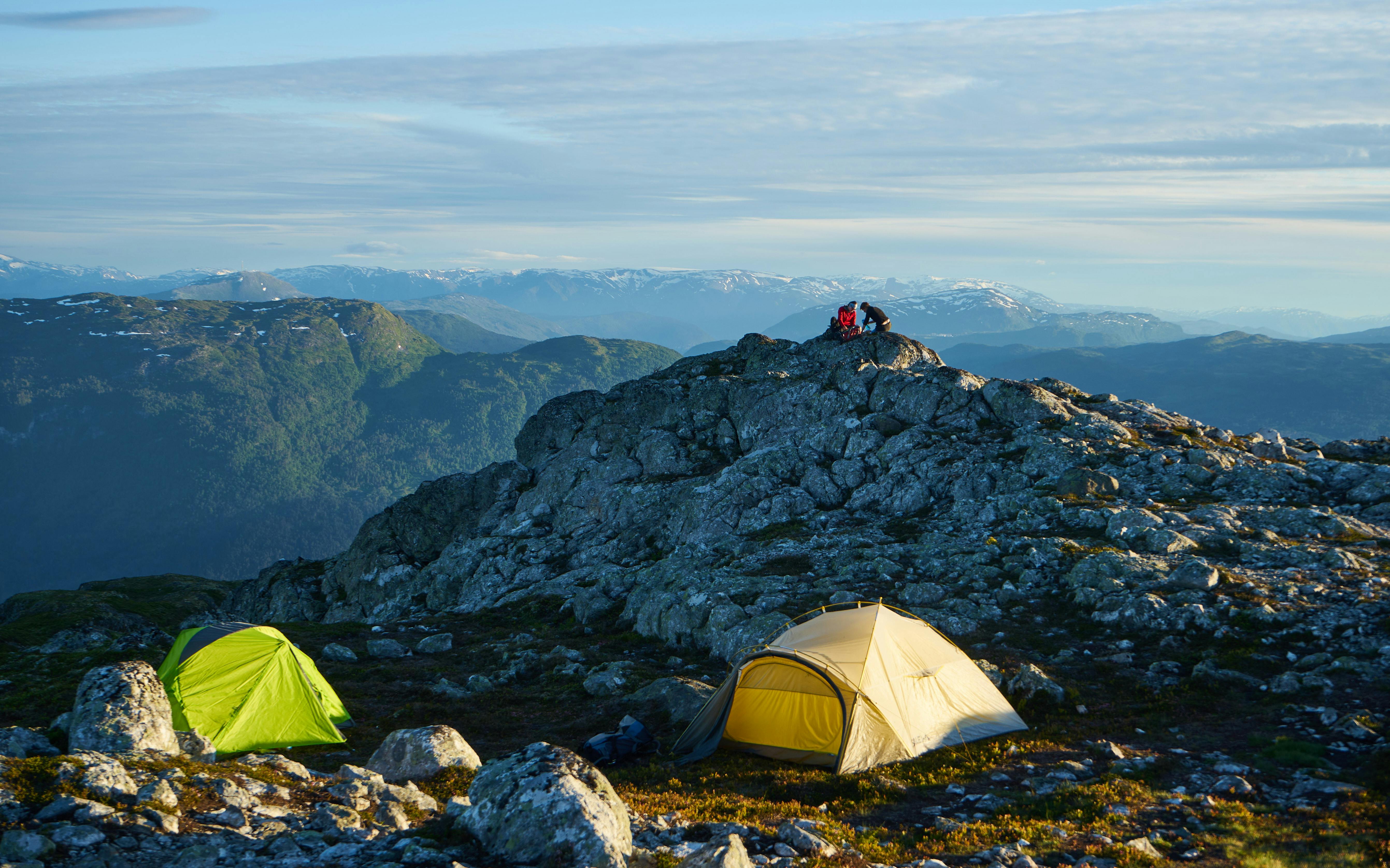 A captivating mountain camping scene with tents and rocky terrain under a clear sky.