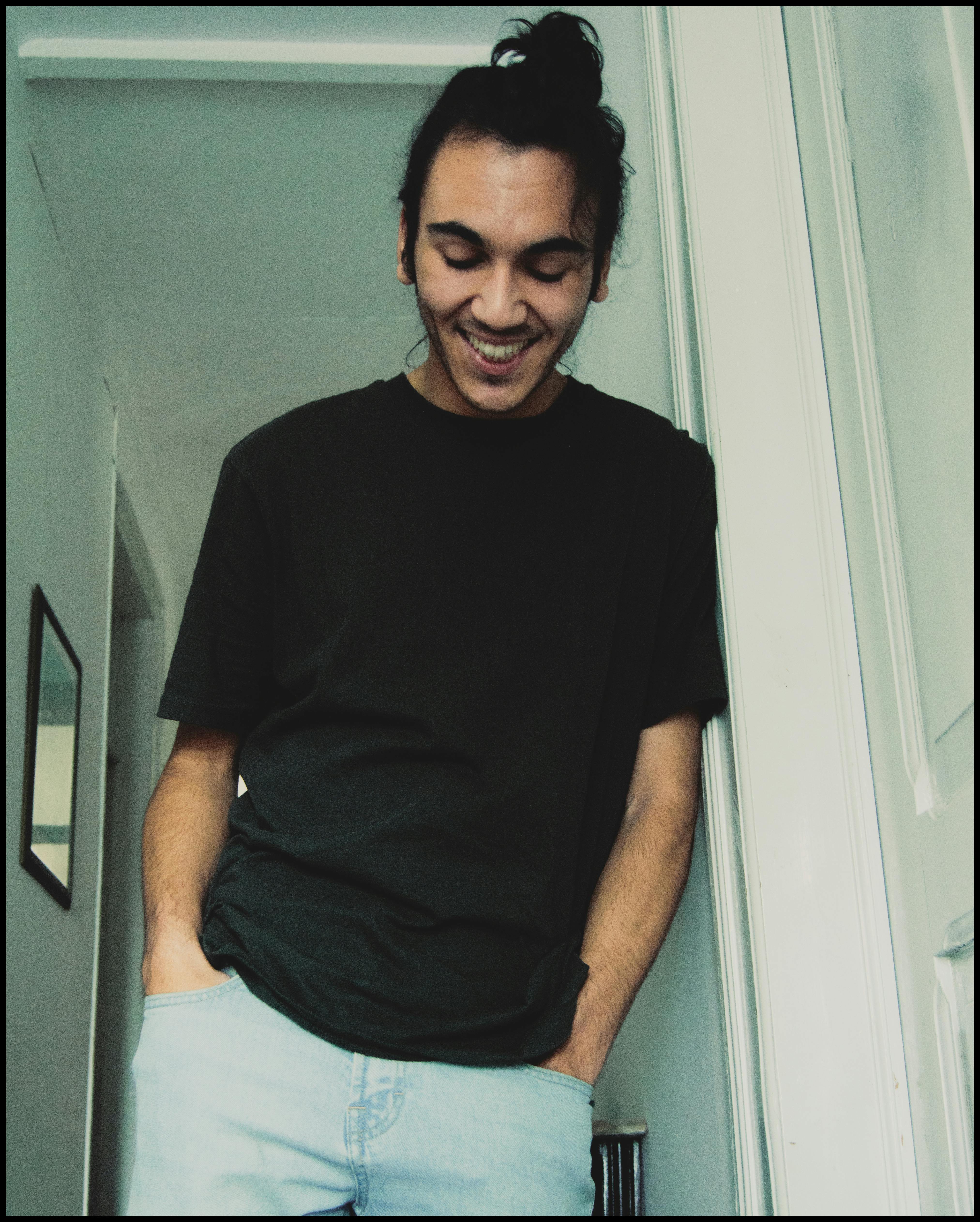 A stylish man in a black t-shirt smiling while standing indoors.
